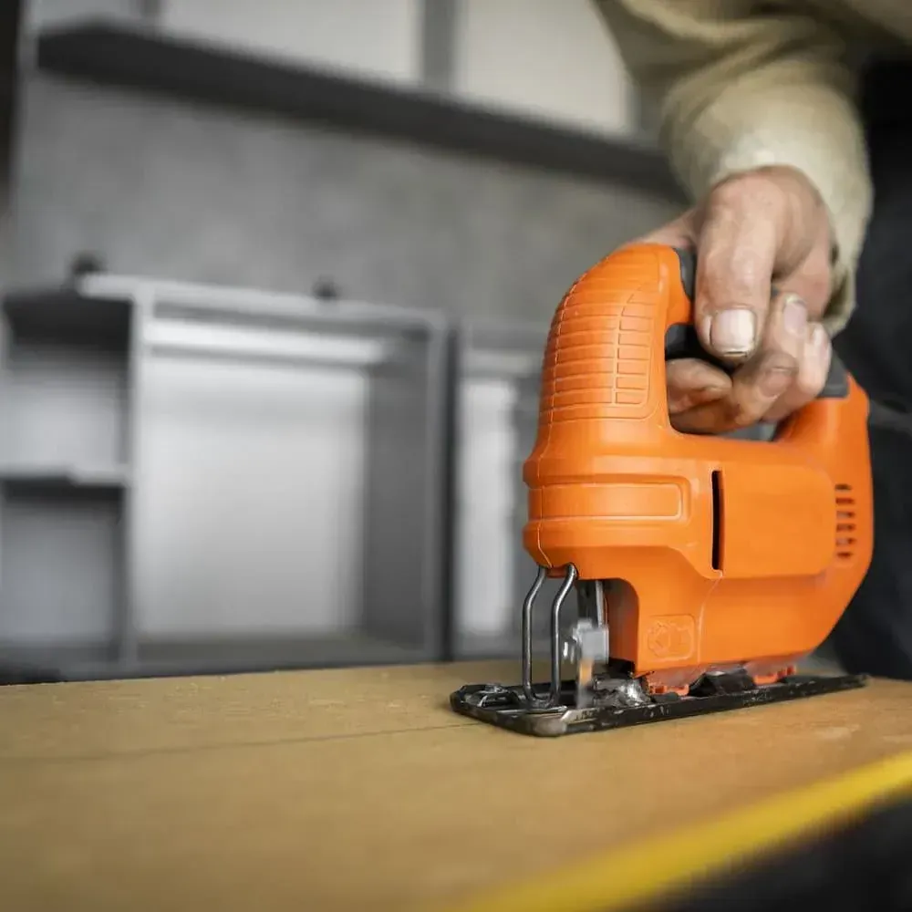 Una persona está usando una sierra caladora naranja para cortar un trozo de madera.