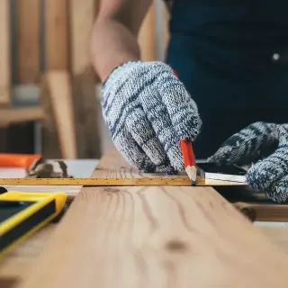 Una persona está midiendo un trozo de madera con una regla y un lápiz.