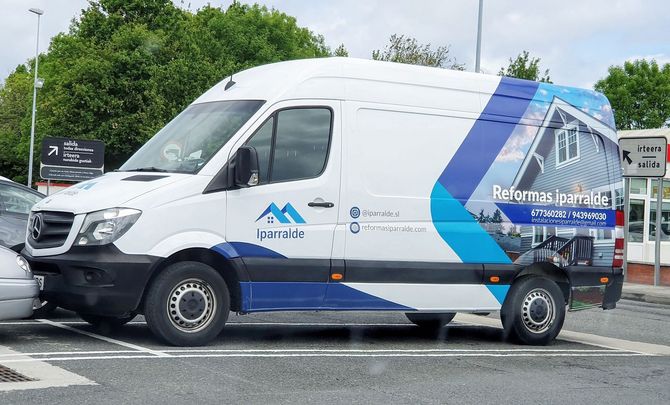 Furgoneta blanca con gráficos azules aparcada en un parking. Anuncio de