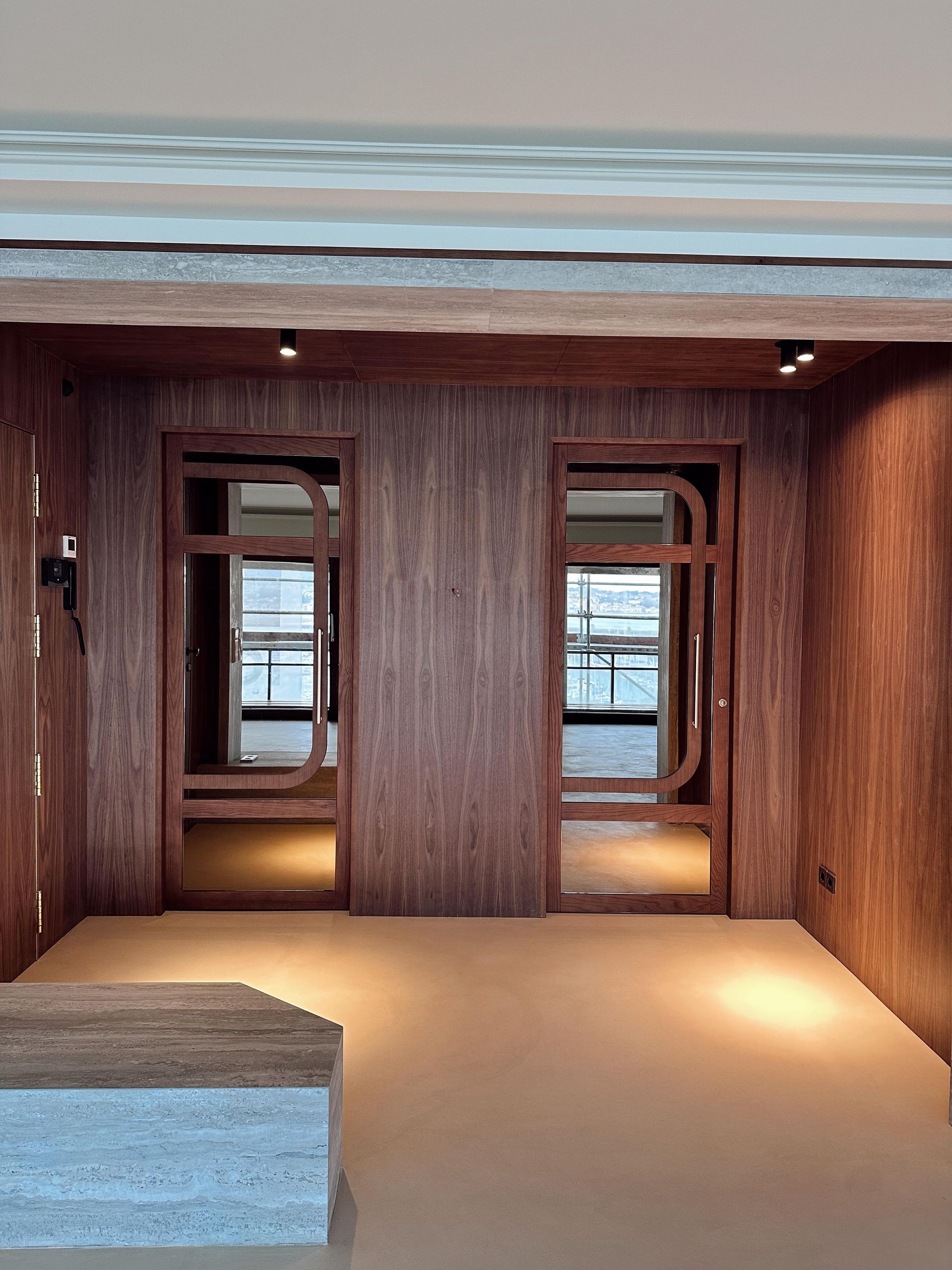 Dos puertas con paneles de madera y espejos dan a un suelo de color beige claro. Focos iluminan el espacio.