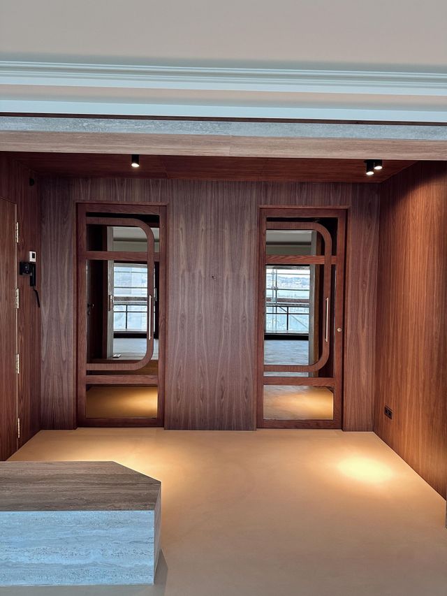 Dos puertas con paneles de madera y espejos dan a un suelo de color beige claro. Focos iluminan el espacio.