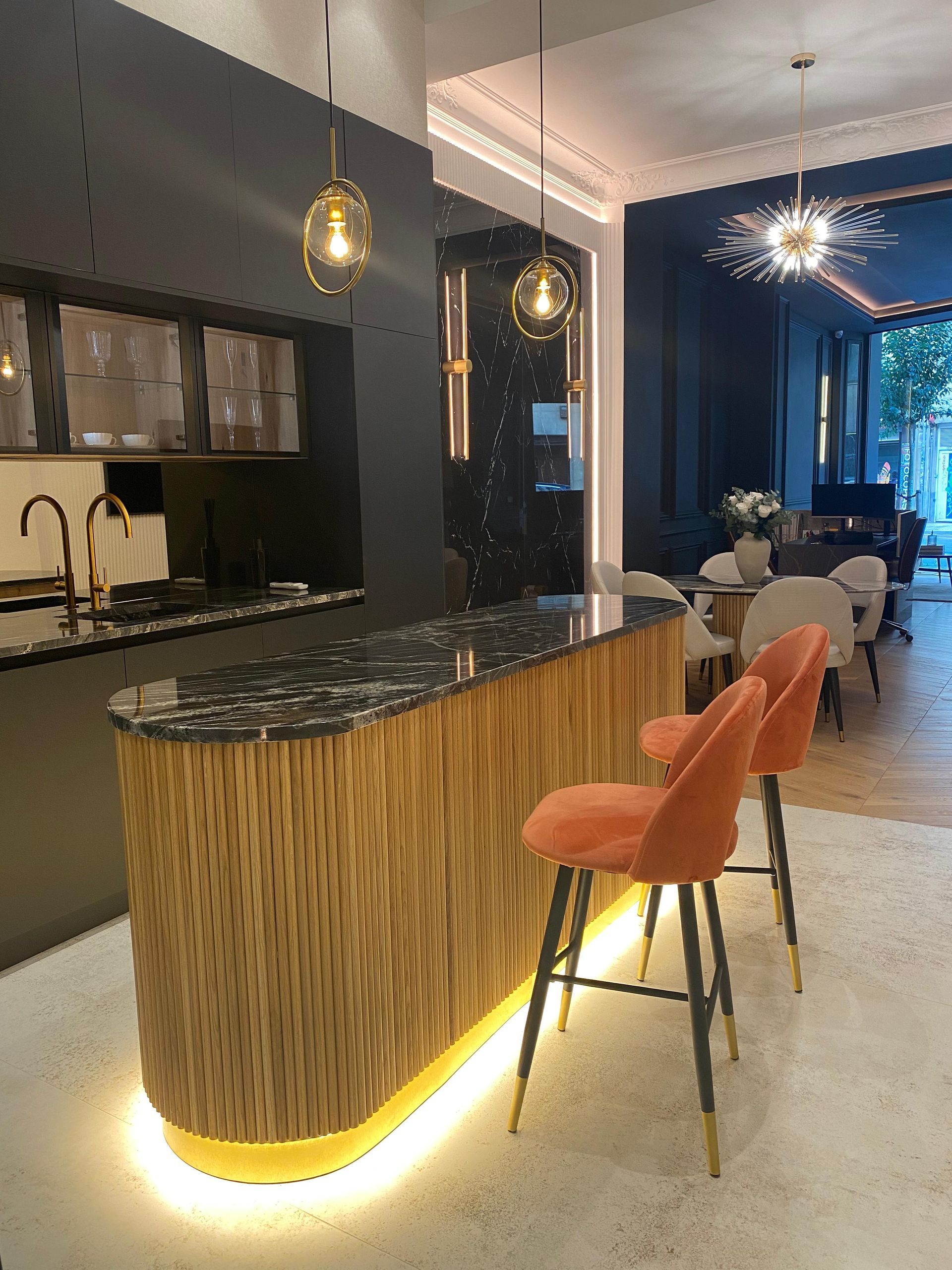 Una cocina moderna con barra de madera, taburetes naranjas y dos lámparas colgantes.