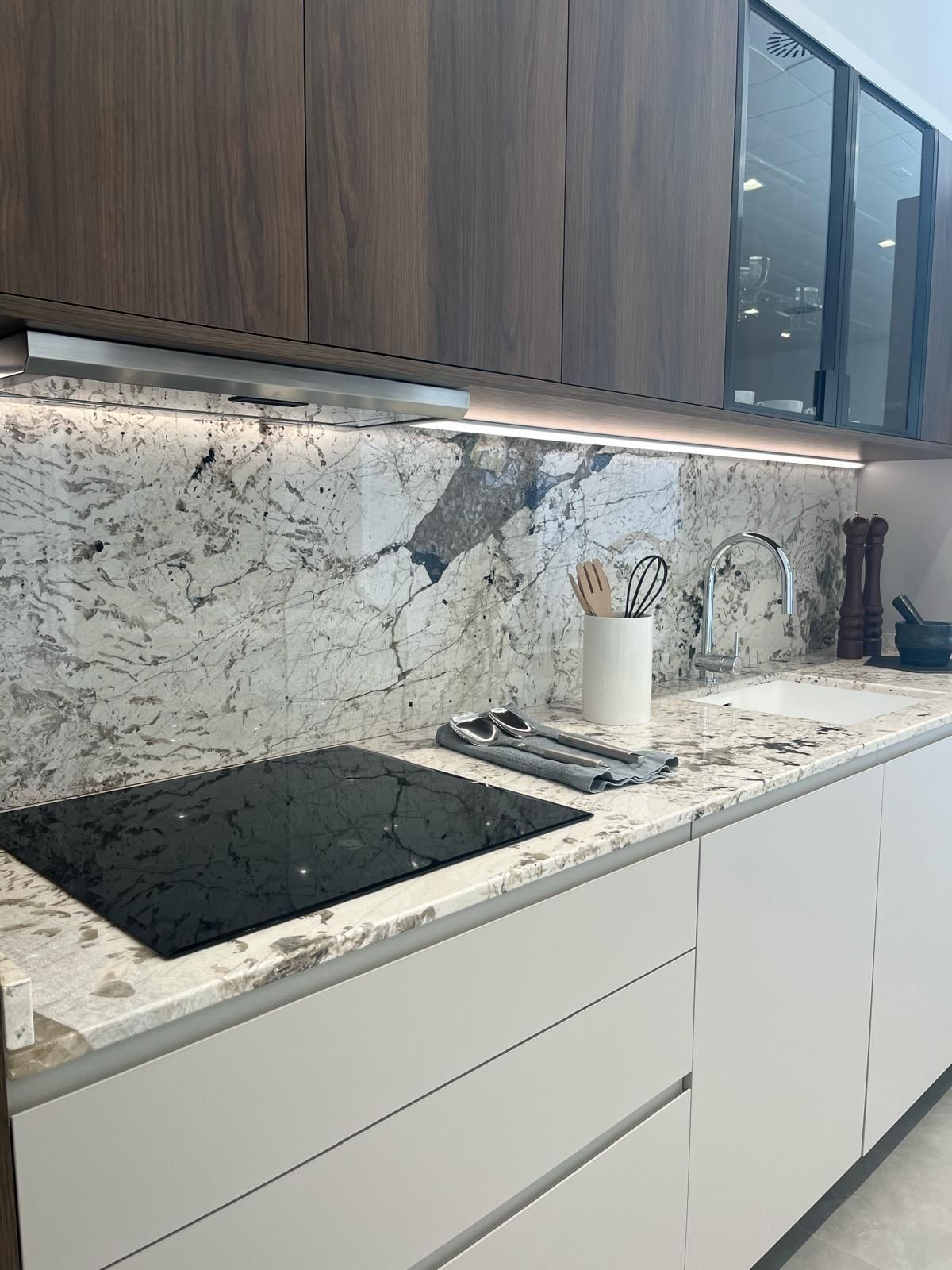 Cocina moderna con armarios blancos, salpicadero de mármol y armarios superiores de madera.