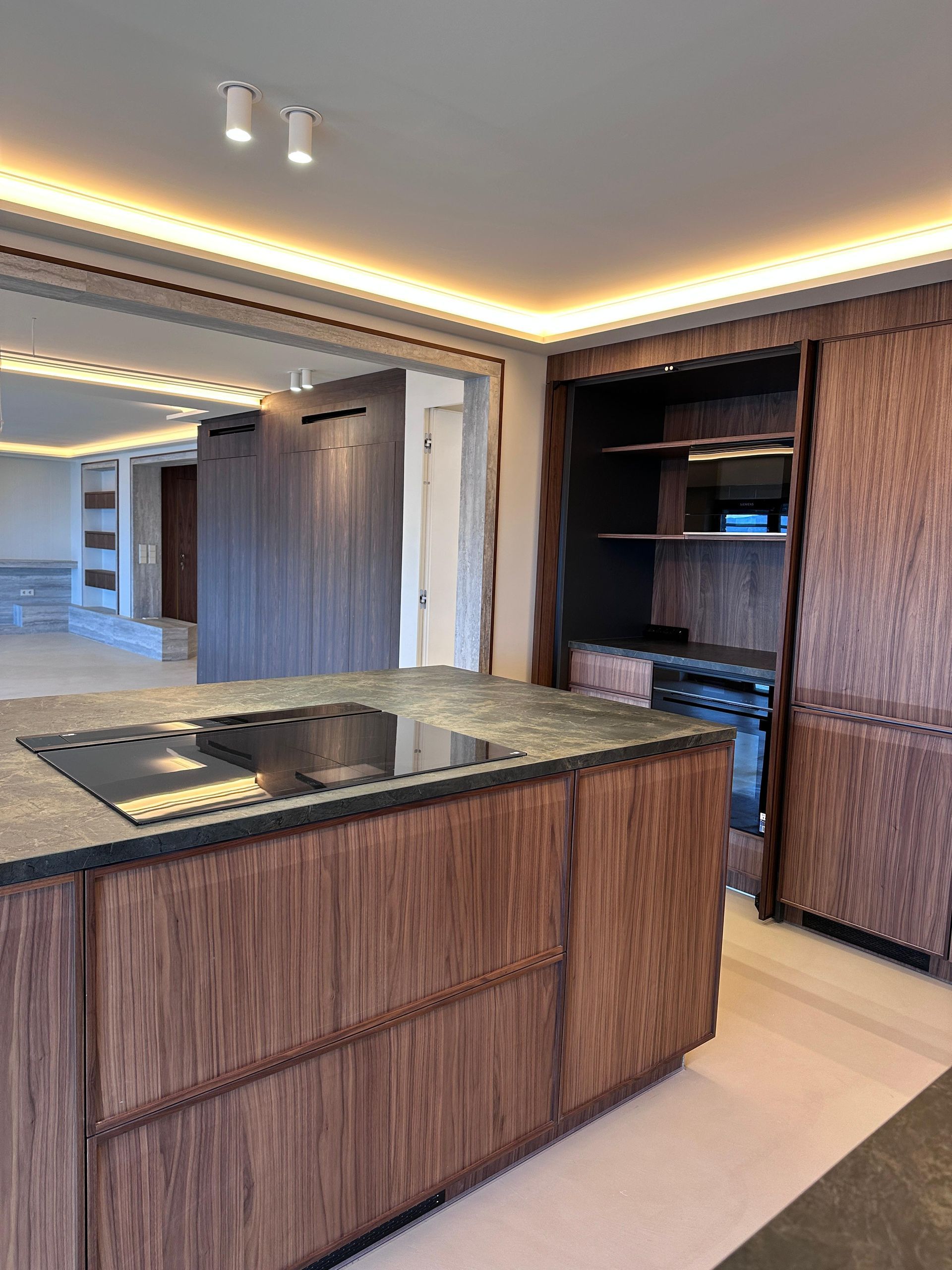 Cocina moderna con gabinetes de madera, isla y placa de cocción. Iluminación superior.