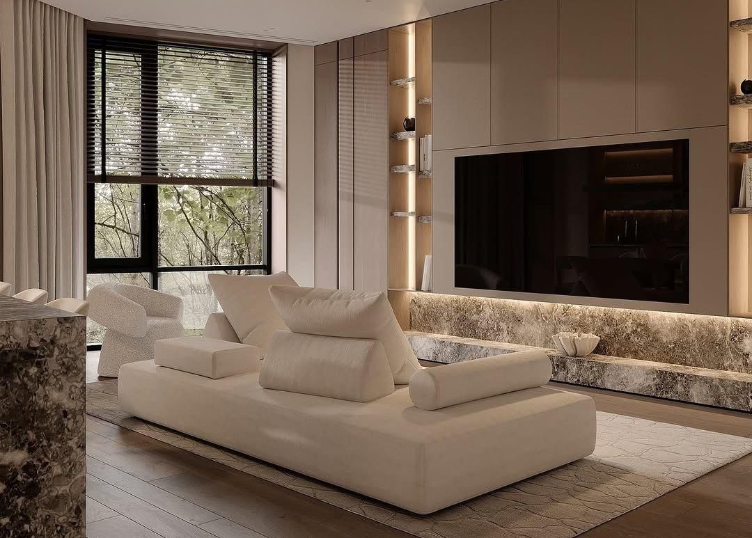 Salón moderno con sofá blanco, televisor grande y ventana con persianas. Tonos neutros.