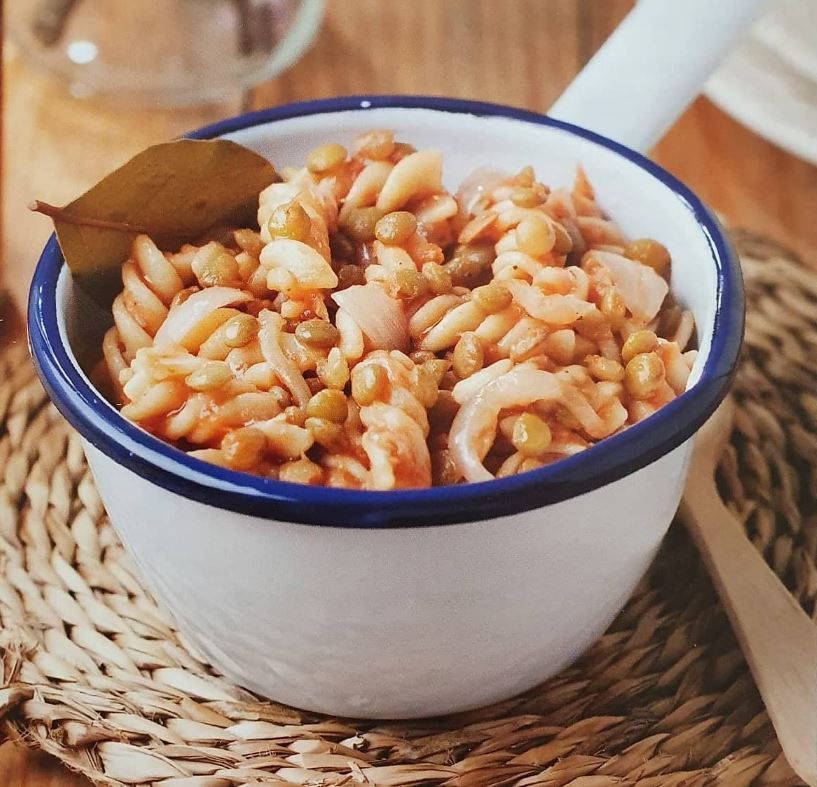 Un tazón de pasta y frijoles con una cuchara dentro.