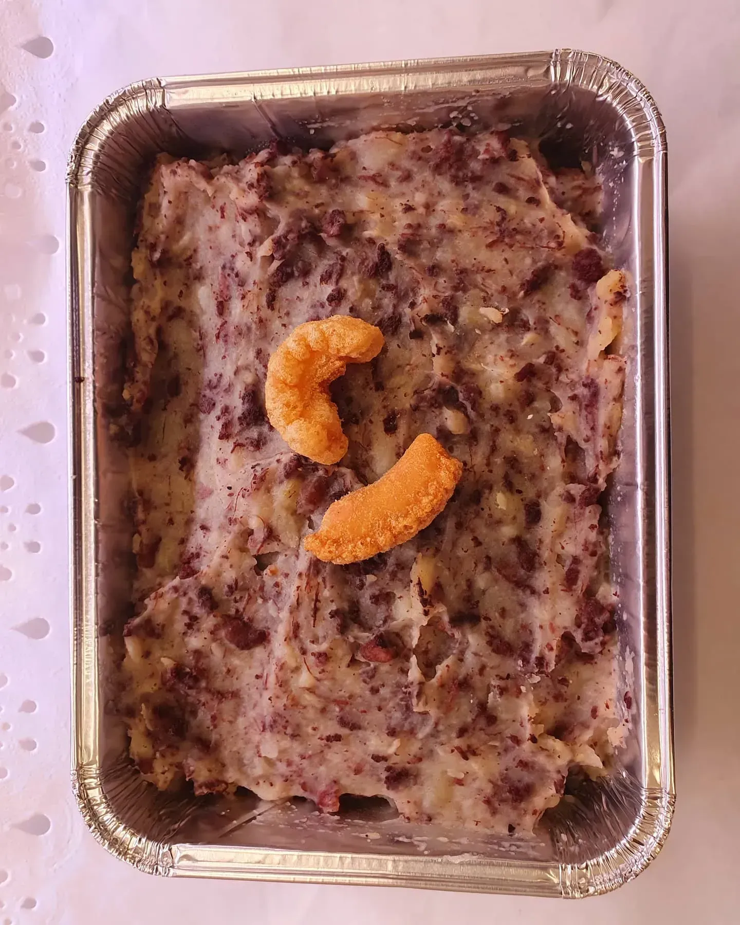 Un recipiente de papel de aluminio lleno de comida con un trozo de queso encima.