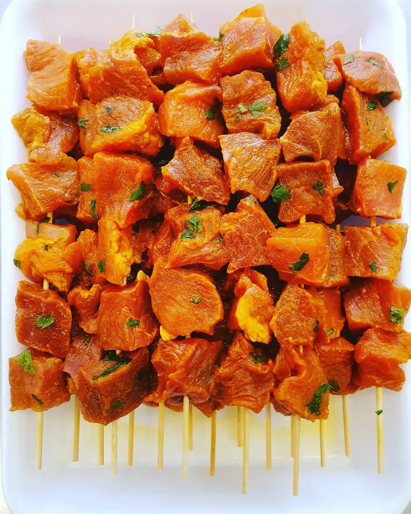 Una bandeja blanca llena de cubos de carne en brochetas.