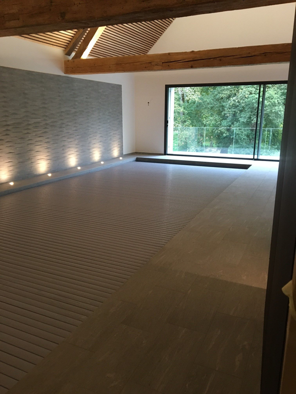 Chambre spacieuse avec sol à motifs, mur en pierre, grande fenêtre et poutres en bois.