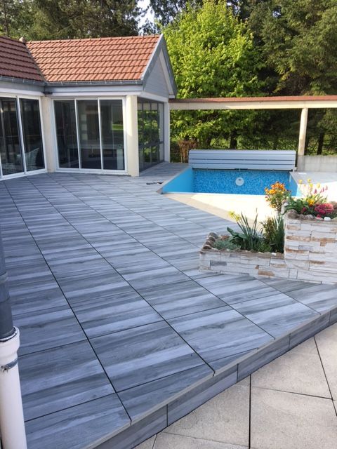 Patio en dalles de pierre grise, menant à une piscine aux dalles bleues, à côté d'un bâtiment aux parois de verre.