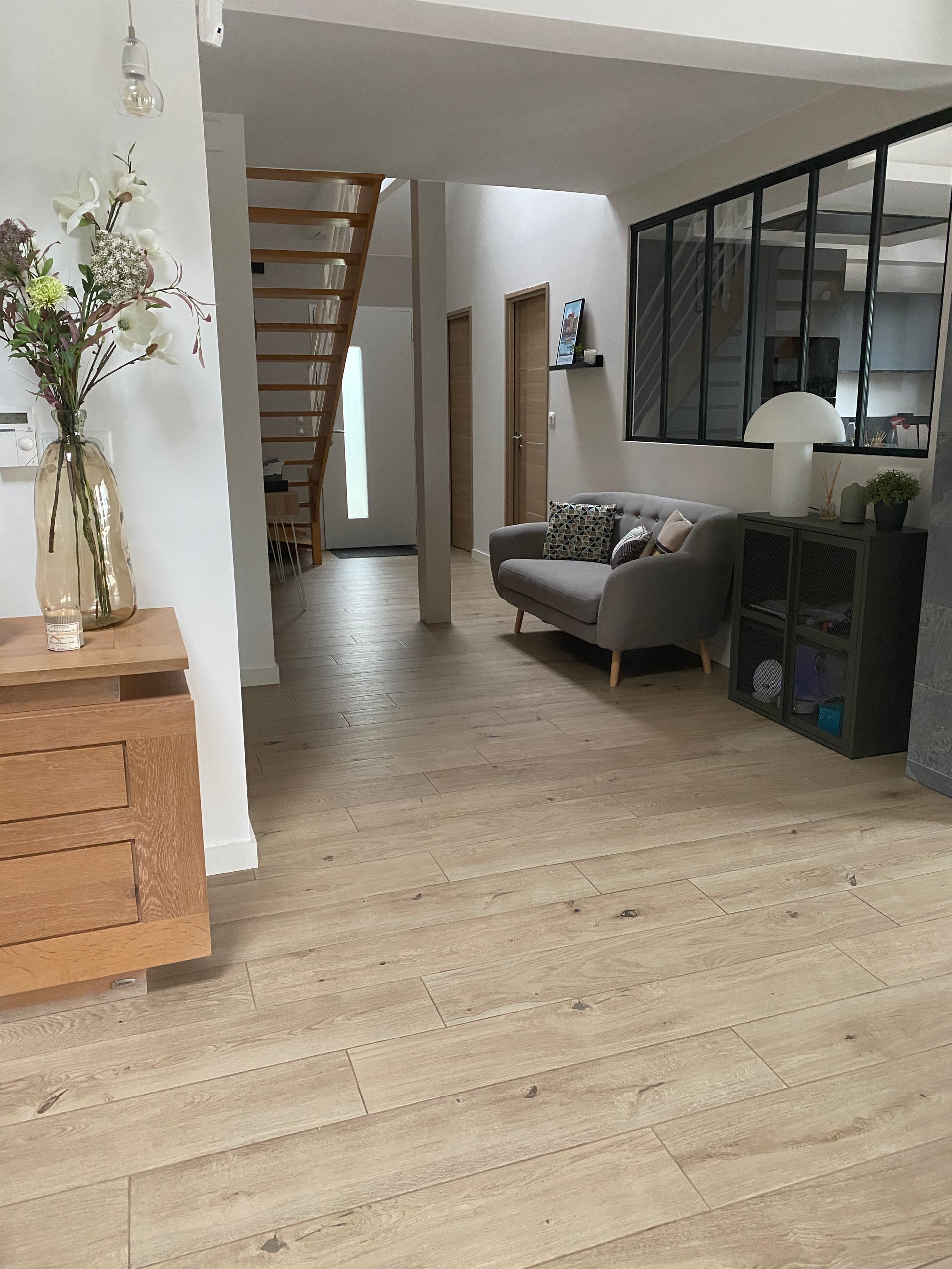 Intérieur spacieux et moderne avec parquet en bois clair, escalier et un petit coin salon.