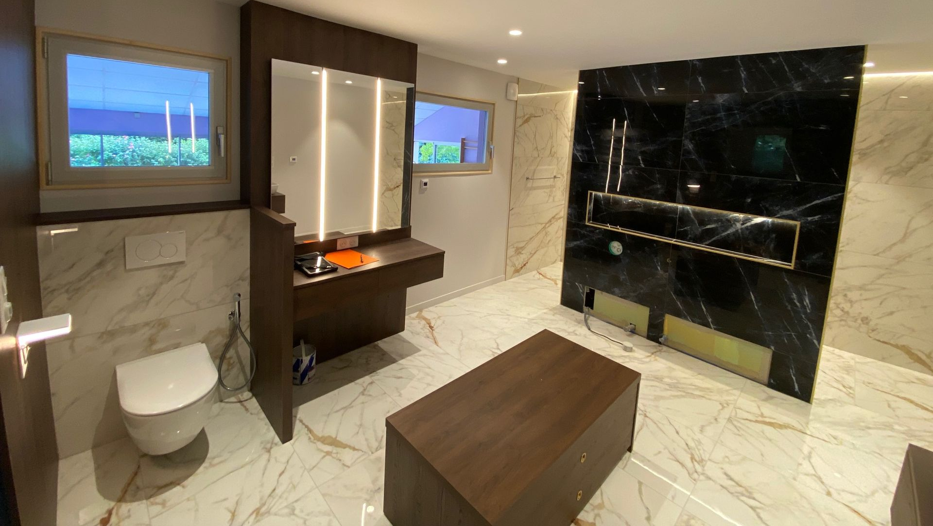 Salle de bains moderne en marbre et bois foncé, comprenant une vanité, des toilettes et un panneau de douche.