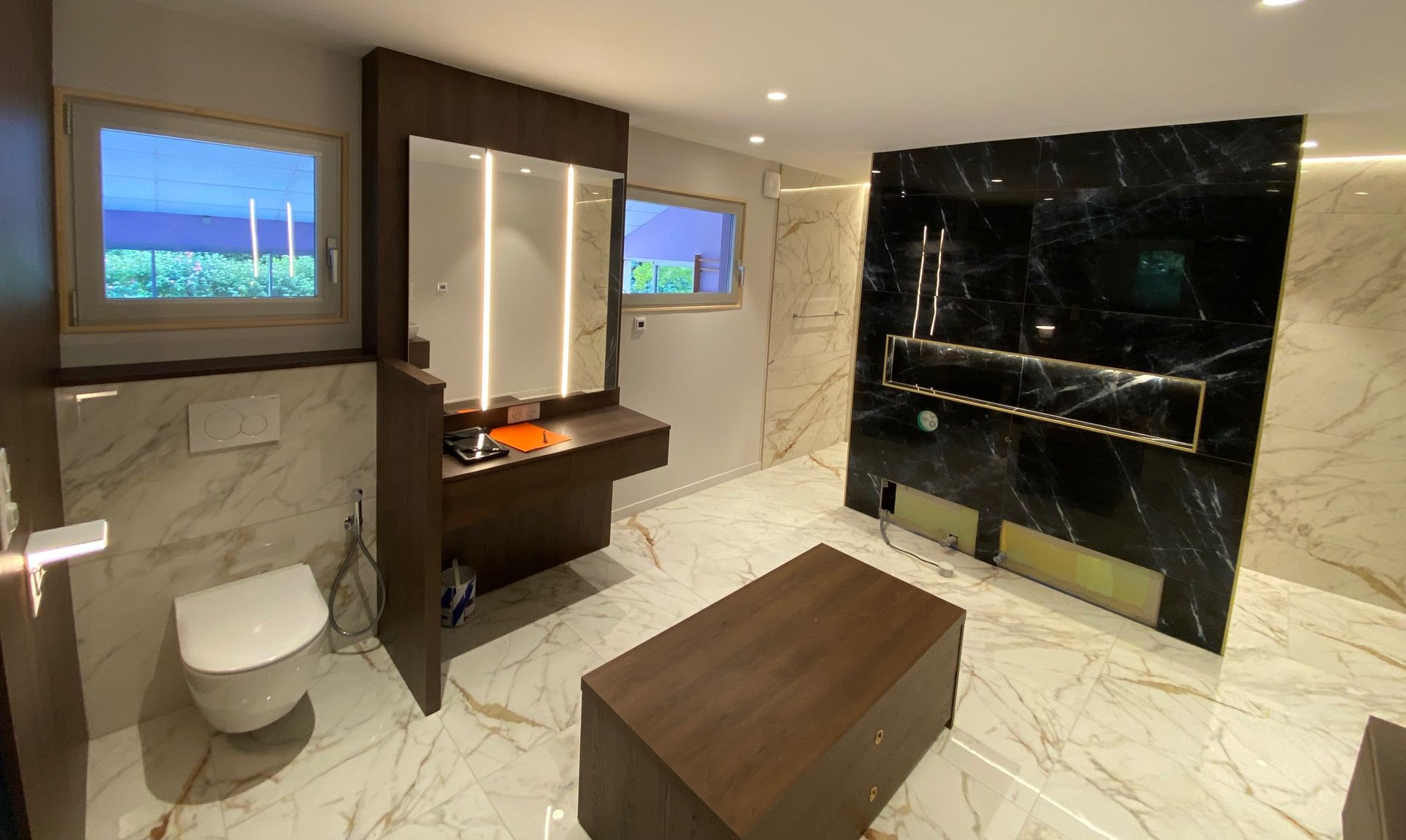 Salle de bains moderne avec carrelage en marbre, vanité marron foncé, paroi de douche noire et toilettes.