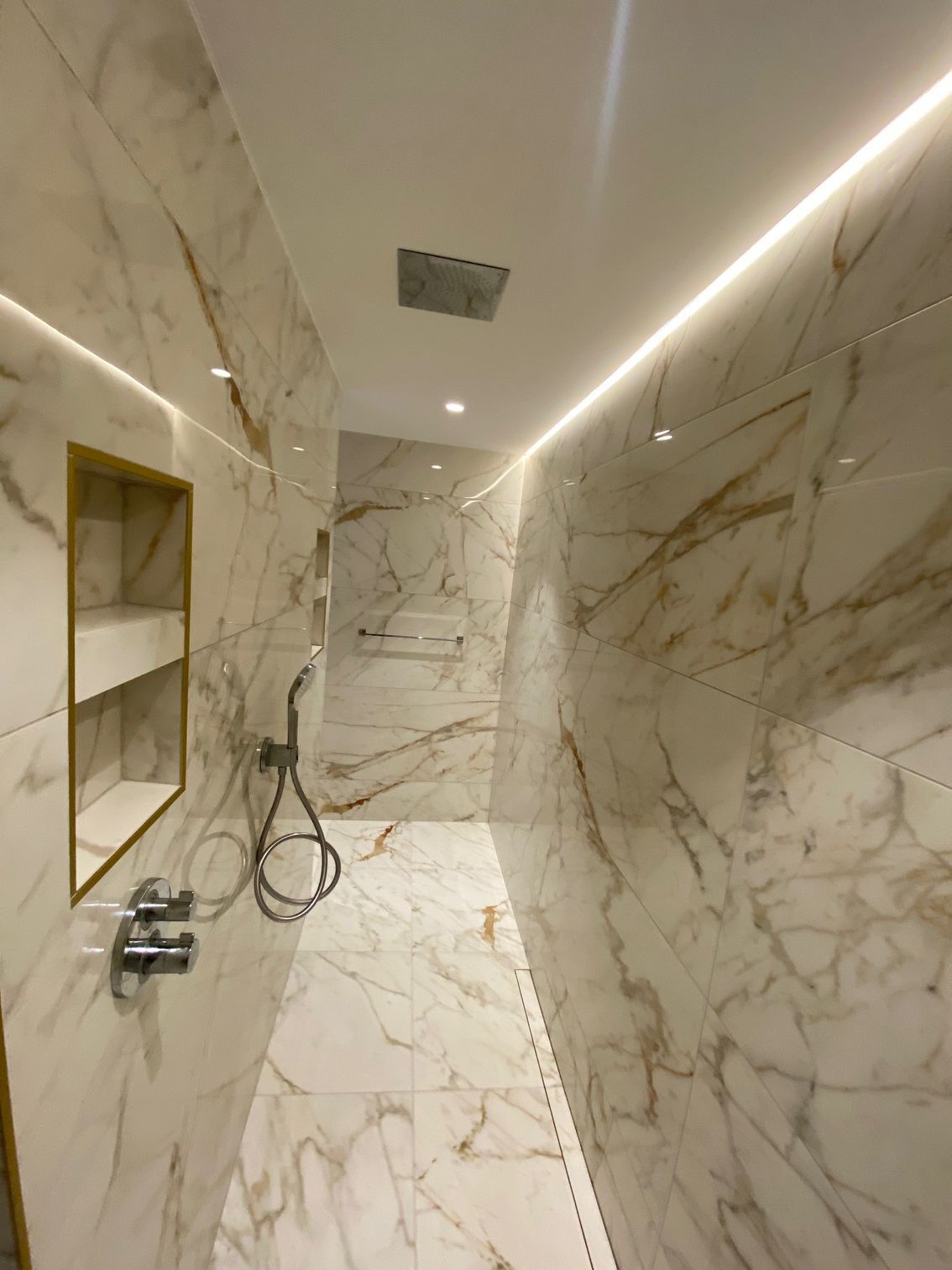 Douche carrelée en marbre avec accents dorés, étagère intégrée, éclairage encastré.