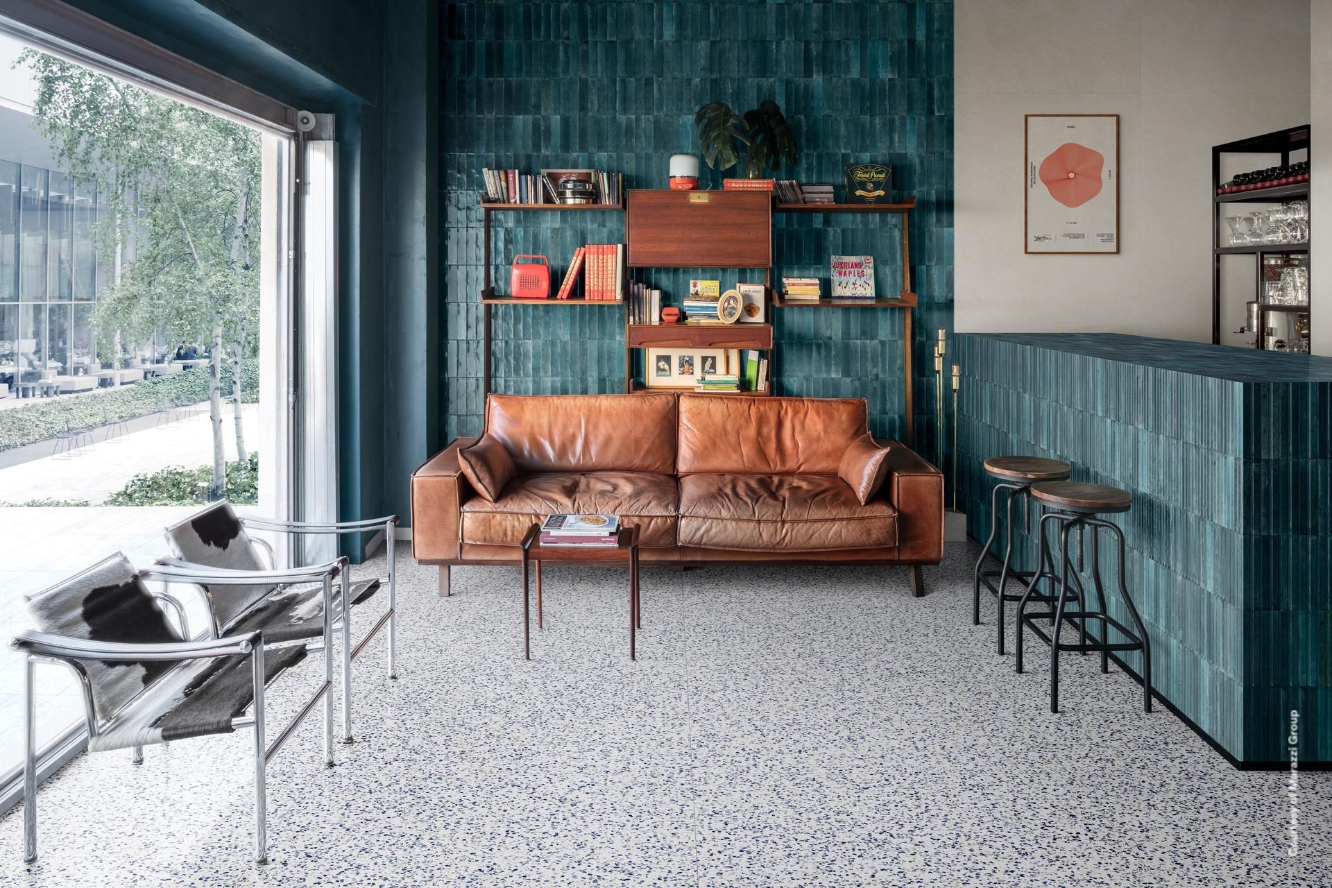 Un café moderne avec un canapé en cuir marron, des murs carrelés bleus, des sols en terrazzo et une vue sur l'extérieur.