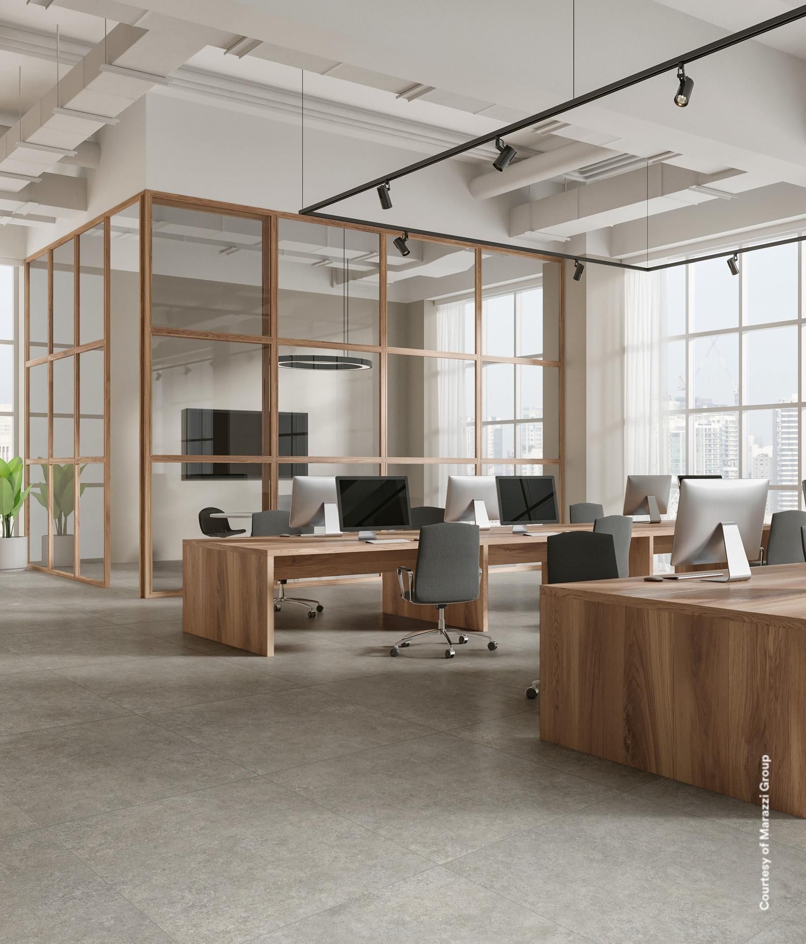 Espace de bureau moderne avec bureaux en bois, cloisons vitrées et ordinateurs. Sol en béton gris, murs blancs.