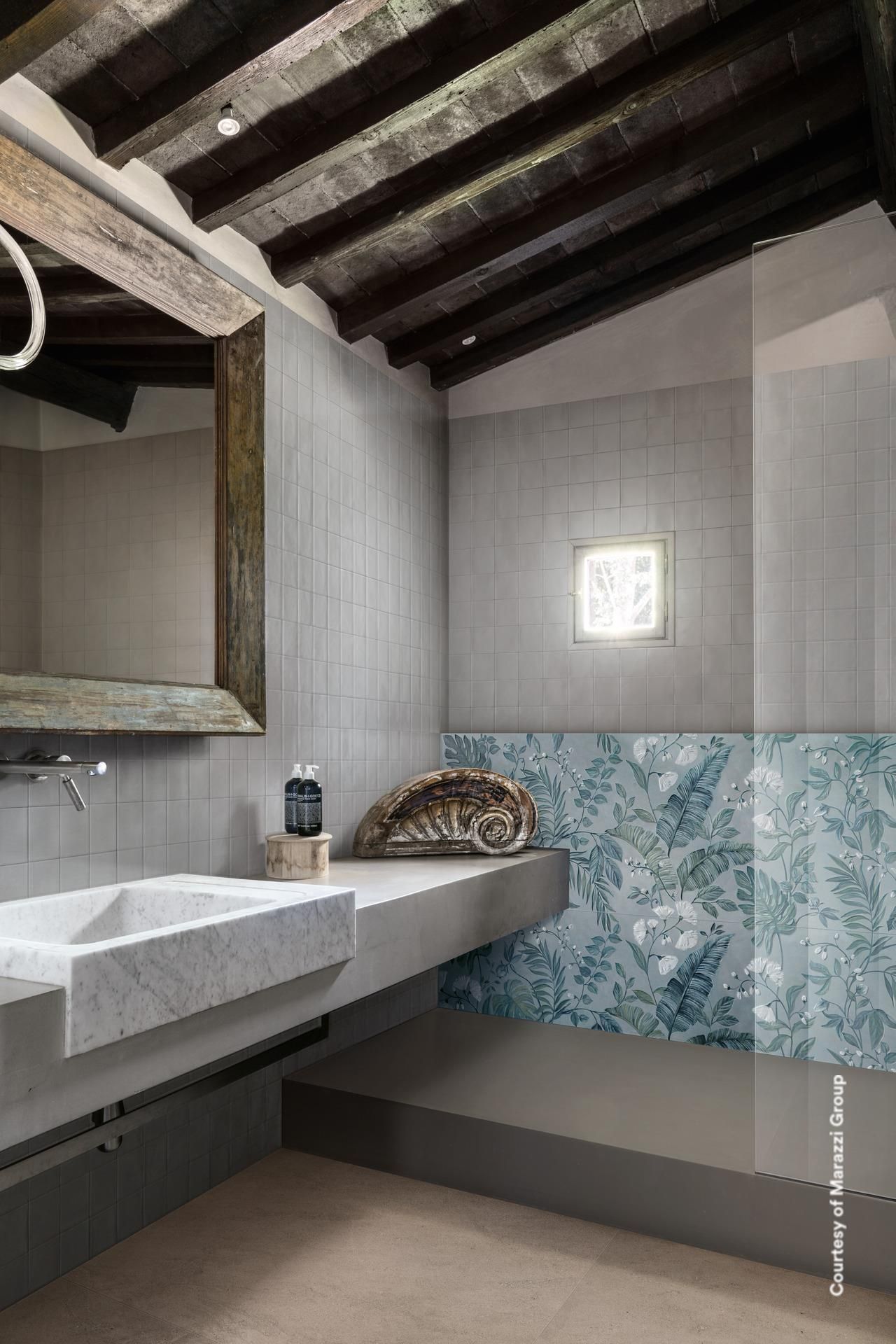 Salle de bain avec lavabo en pierre, accent de carrelage floral bleu, poutres en bois au plafond et miroir rustique.