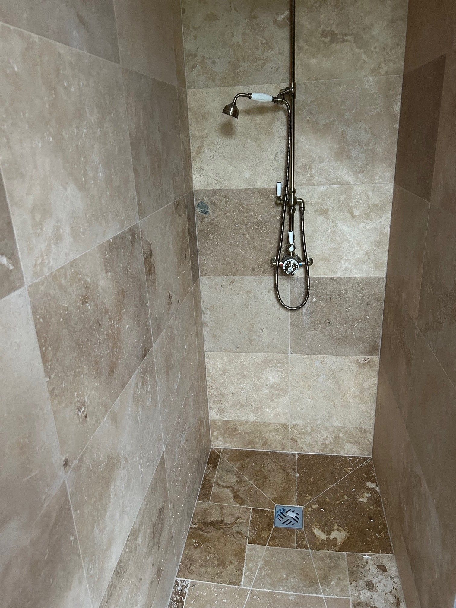 Cabine de douche avec carrelage marron clair aux murs et au sol. Pommeau et robinet chromés.