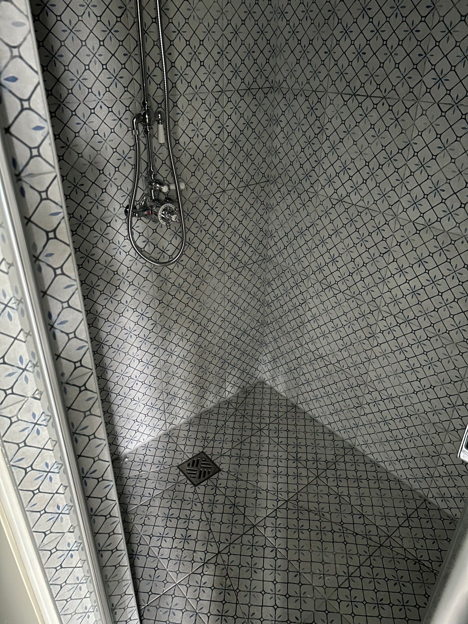 Intérieur de douche avec carrelage à motifs gris et blanc, pomme de douche et drain chromés.
