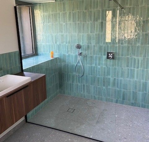 Salle de bains avec carrelage vertical bleu sarcelle, douche, vanité en bois et fenêtre.