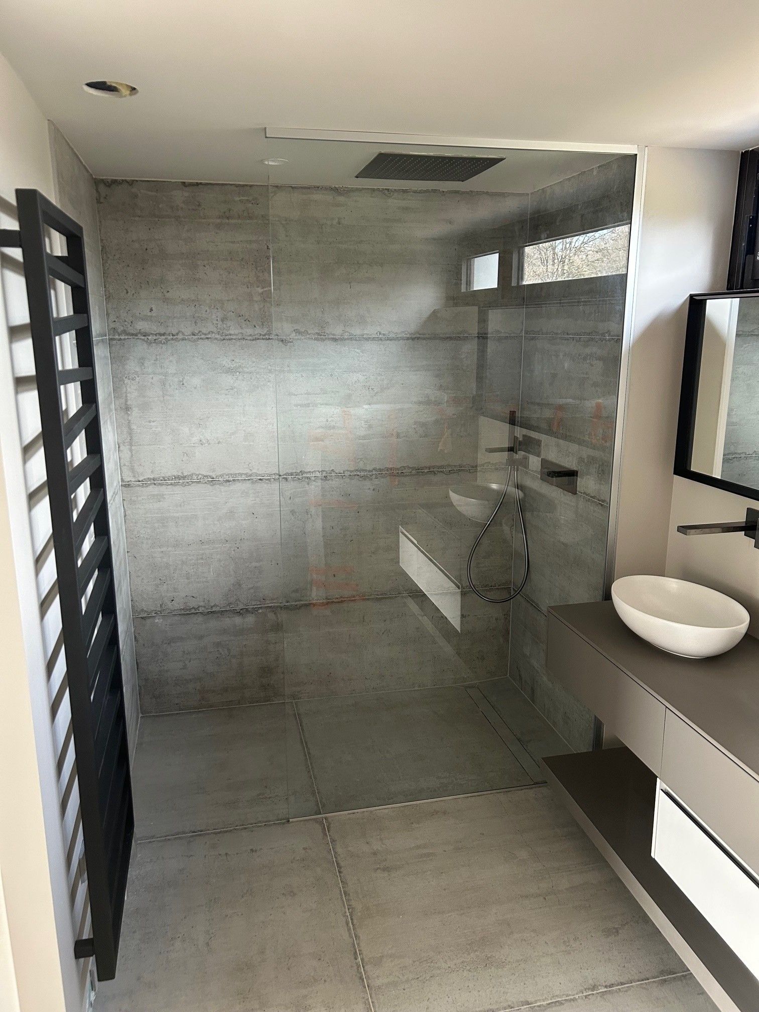 Salle de bains moderne avec carrelage gris, douche en verre et lavabo minimaliste.