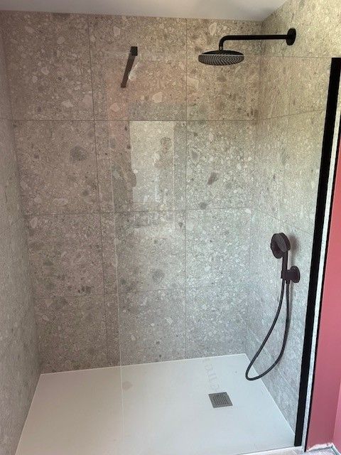 Douche moderne avec murs en carrelage de pierre grise, luminaires noirs et base blanche.