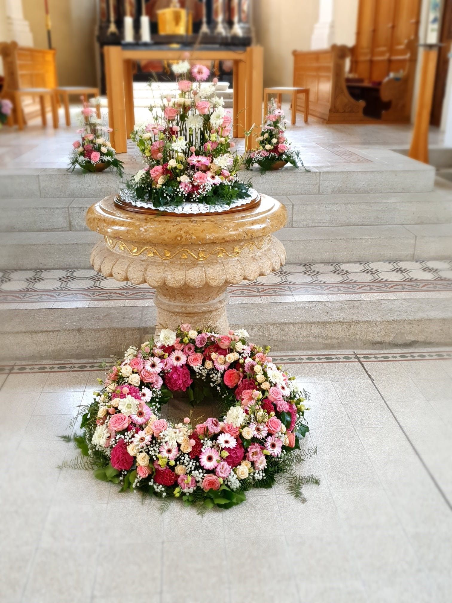 Ein mit Blumen und einem Kranz geschmücktes Taufbecken in einer Kirche.