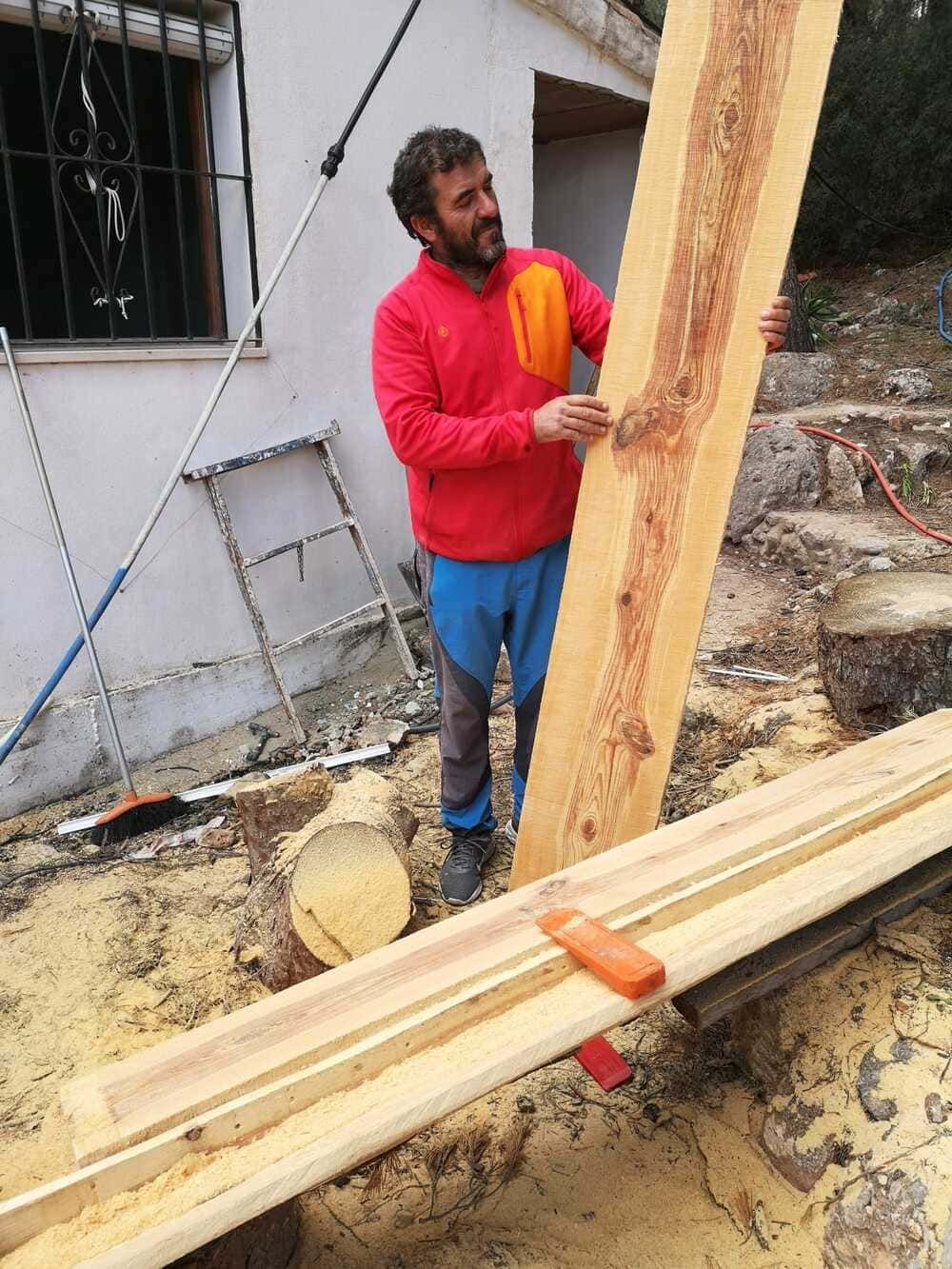 Un hombre con una camisa roja sostiene un gran trozo de madera.