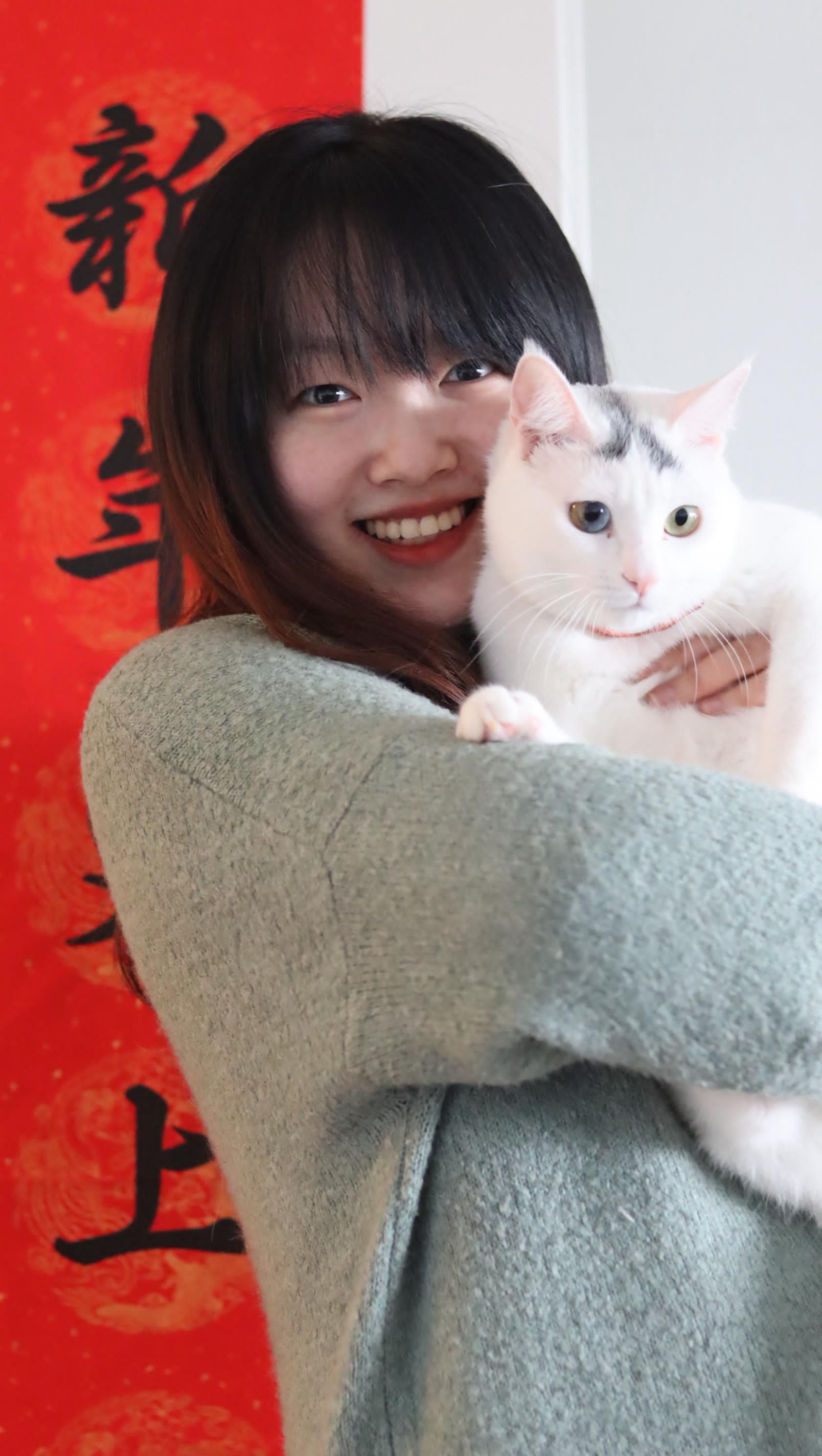 Frau lächelt und hält eine weiße Katze vor roter Dekoration zum chinesischen Neujahr.