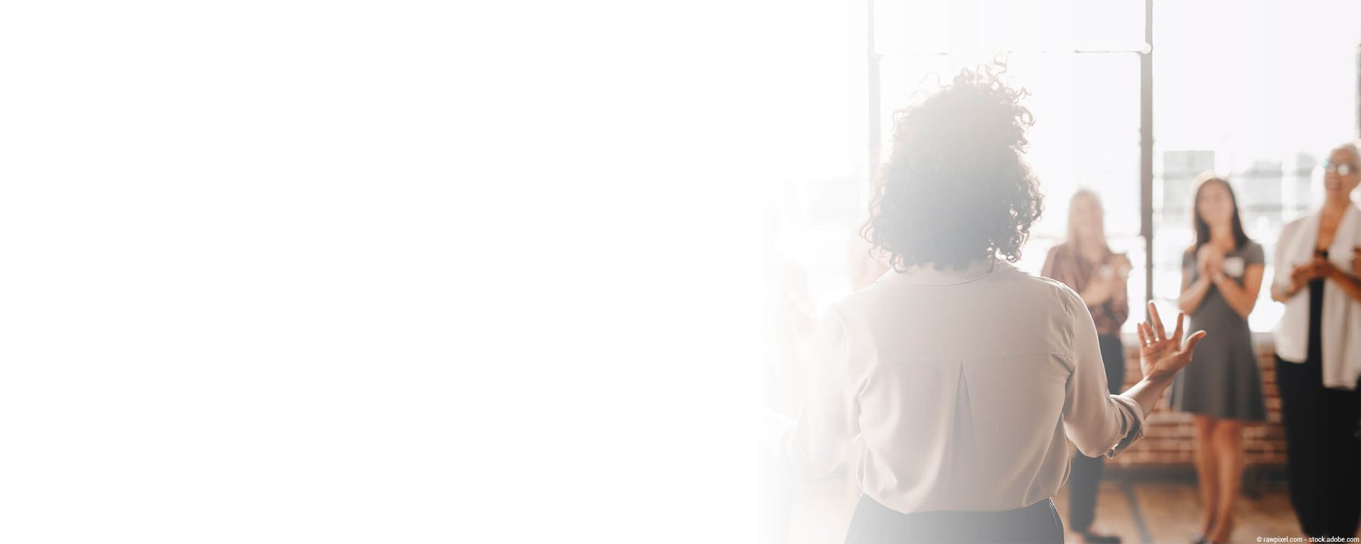 Eine Person hält eine Präsentation, während andere klatschen; drinnen, Licht fällt durch die Fenster.