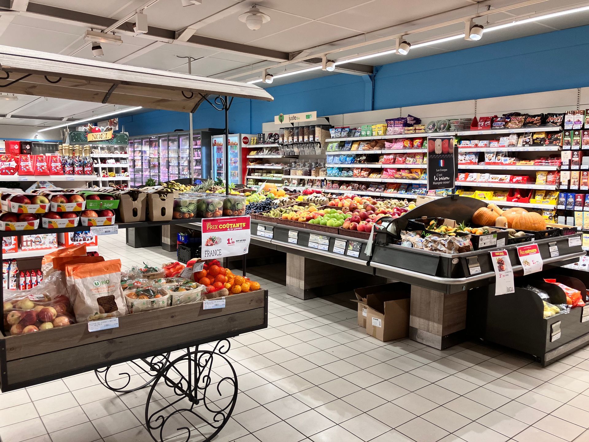 Intérieur du supermarché avec des étals de fruits et légumes et des rayons de produits
