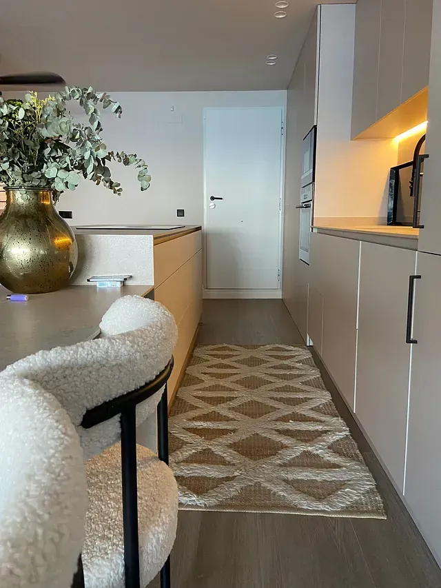 Una cocina con una alfombra y sillas y un jarrón de flores en la encimera.
