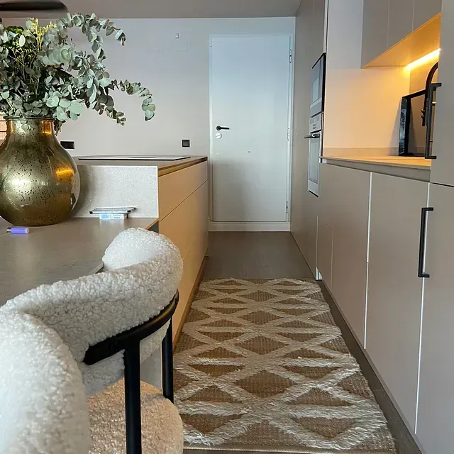 Una cocina con una silla y un jarrón de flores sobre la mesa.