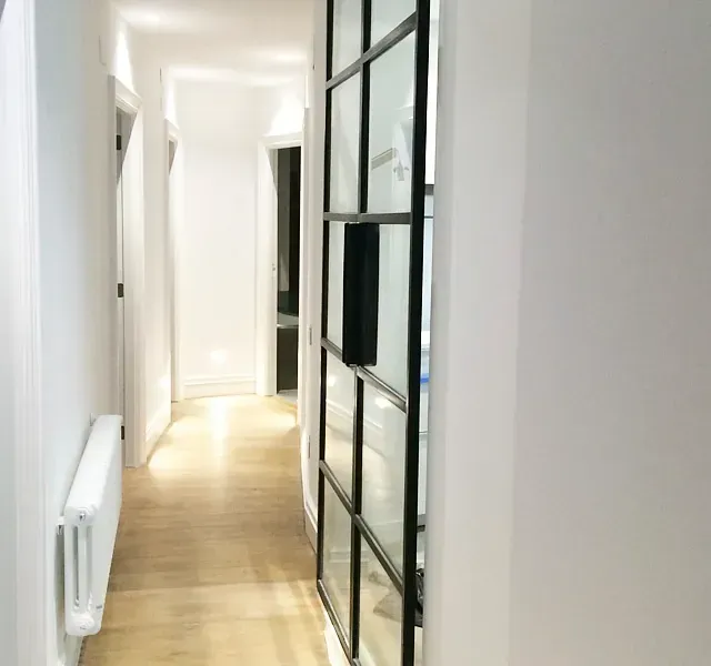 Un largo pasillo con un radiador y una puerta corrediza de cristal.