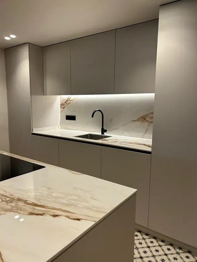 Una cocina con gabinetes blancos, encimeras de mármol y un fregadero.