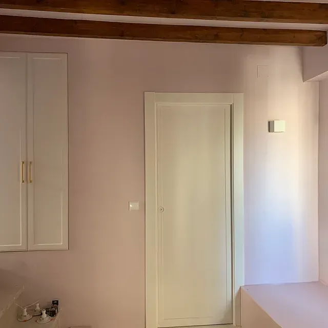 Un baño con paredes rosas, armarios blancos y una puerta blanca.