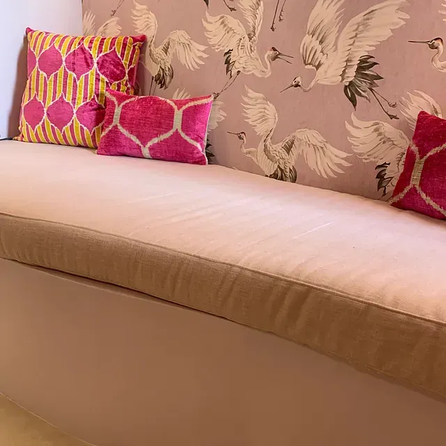 Un sofá con cojines rosas y amarillos frente a una pared con pájaros.