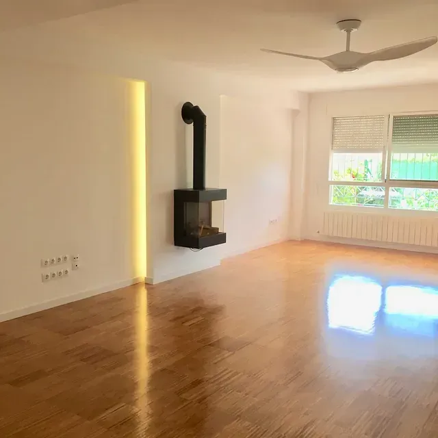 Una sala de estar vacía con pisos de madera y un ventilador de techo.