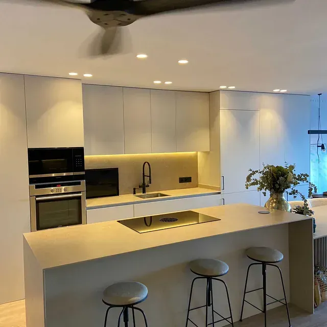 Una cocina con gabinetes y taburetes blancos y un ventilador de techo.