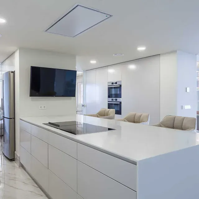 Una cocina con gabinetes blancos y un televisor de pantalla plana en la pared.
