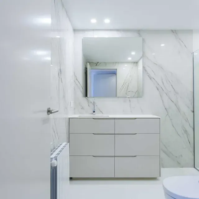 Un baño con lavabo, inodoro, espejo y paredes de mármol.