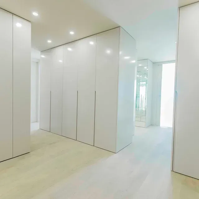 Un pasillo con muchos armarios blancos y un espejo.