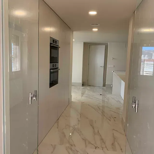 Un pasillo que conduce a una cocina con pisos de mármol y gabinetes blancos.