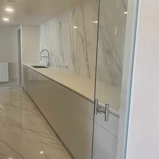 Una cocina con gabinetes blancos, encimeras de mármol, un fregadero y una puerta de vidrio.