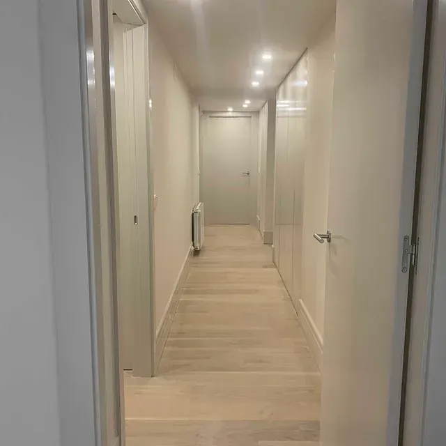 Un largo pasillo con paredes blancas y pisos de madera en una casa.
