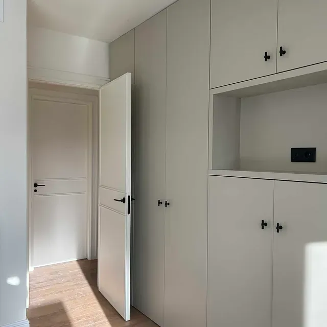 Un pasillo con armarios blancos y una puerta.