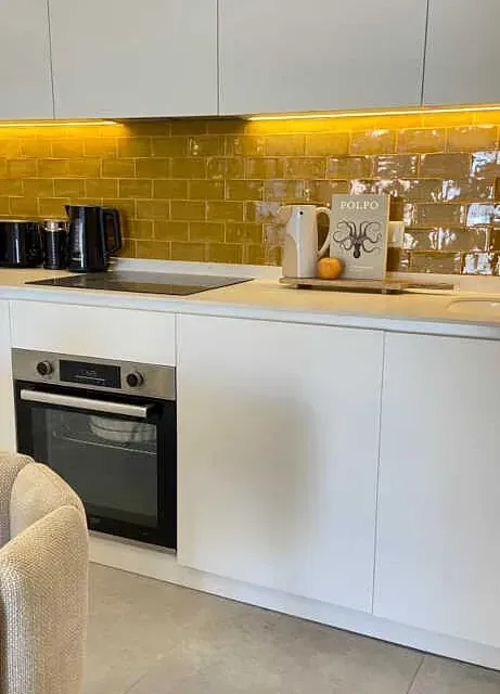 Una cocina con azulejos amarillos, gabinetes blancos, una estufa y un libro en la encimera.