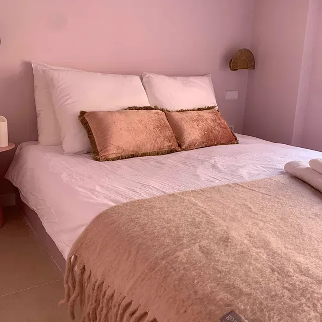 Una cama con una manta y almohadas en un dormitorio rosa.