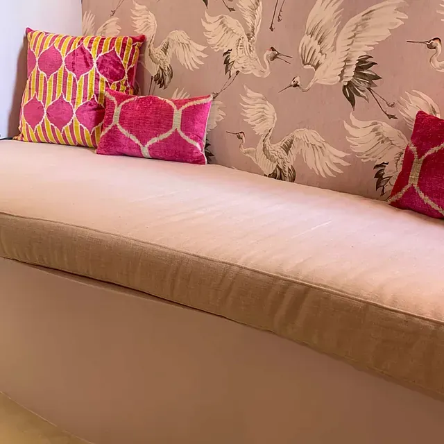 Un sofá con dos almohadas frente a una pared con pájaros.