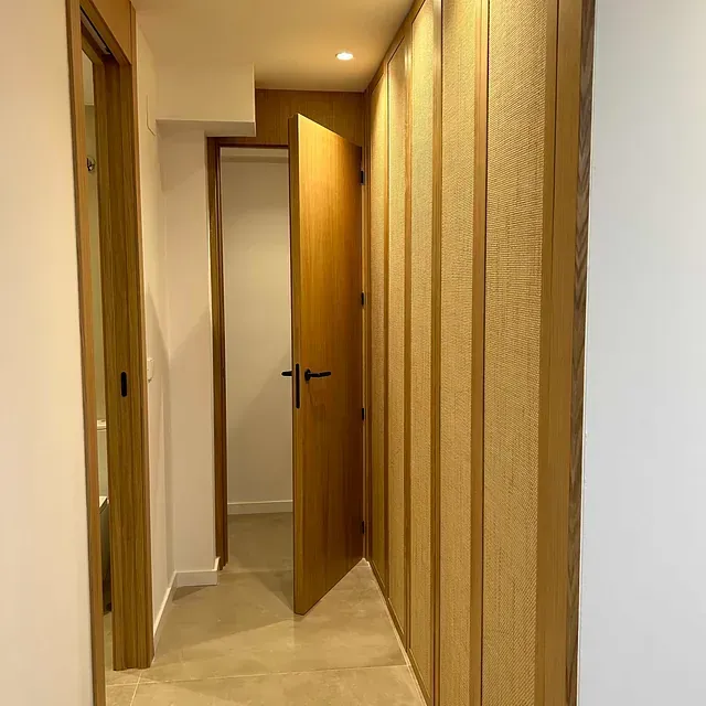 Un pasillo con una puerta de madera y una pared blanca.